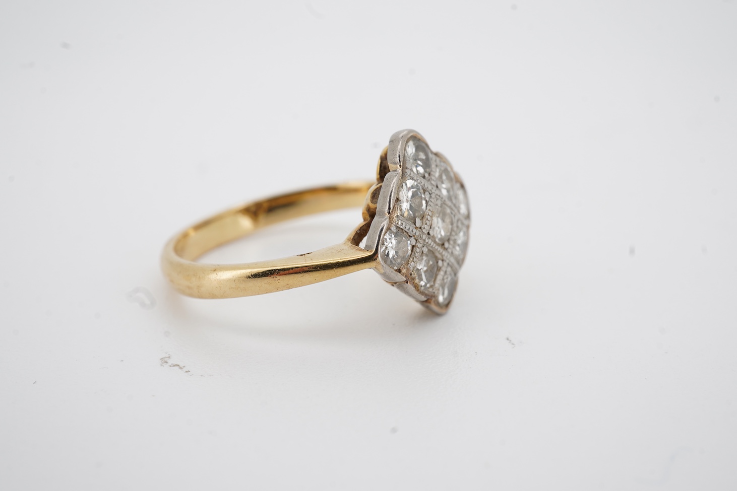 A yellow metal and nine stone millegrain set diamond cluster ring, of diamond form, size M, gross weight 2.9 grams.
